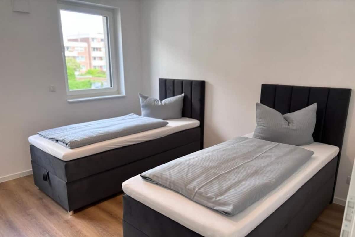 Un dormitorio con dos camas, una ventana y suelo de madera.