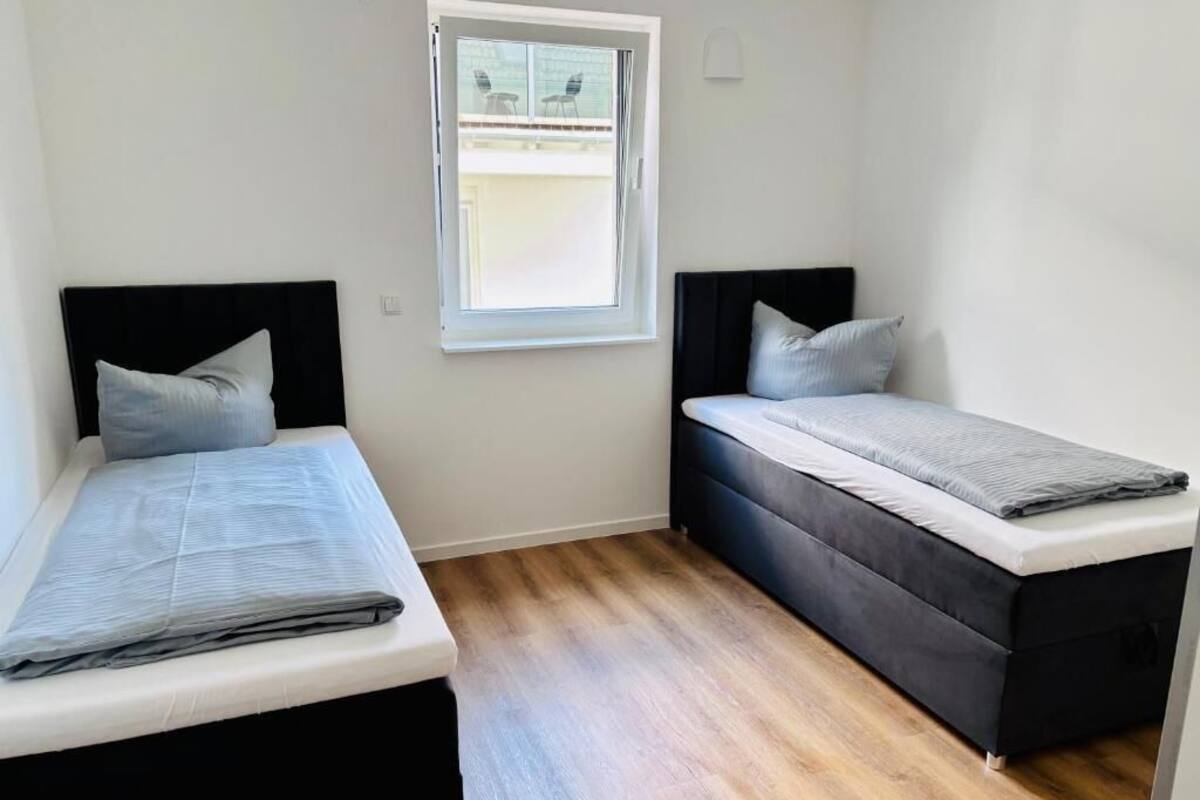 Una habitación pequeña con dos camas, una ventana y piso de madera.