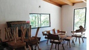 Ein Zimmer mit Holztischen und -stühlen, einem Kamin, großen Fenstern und einer Holzbalkendecke.