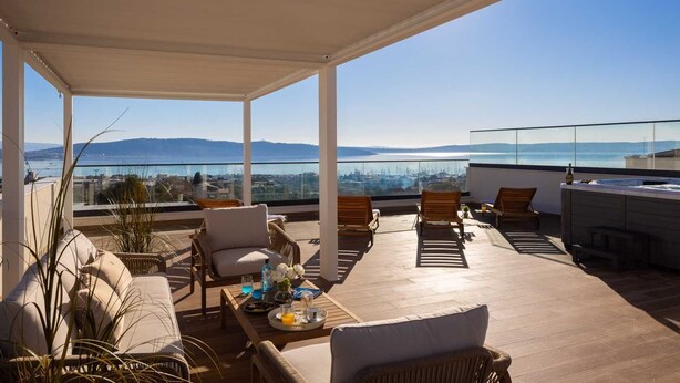 Eine Dachterrasse mit Korbmöbeln, einem Whirlpool und weiter Aussicht auf die Stadt und die Berge.