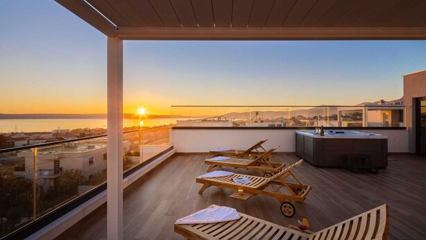 A rooftop terrace with wooden lounge chairs, a bar area, and a view of the sunset over the sea. - Luxury Villa Prime Dalia with Heated Pool (Kaštel Sućurac)
