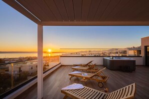En takterrass med trämöbler, en bar och utsikt över solnedgången över havet.