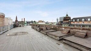 A rooftop terrace with wooden seating and a view of city buildings.