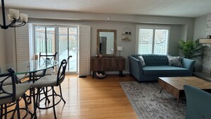 A living room with a blue sofa, a wooden coffee table, and a dining area with a glass table and chairs. - Serene Lake Ontario Retreat • Entire Home Near Trails & Beach. (Ajax)