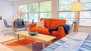 Ett modernt vardagsrum med ett soffbord i trä, en orange soffa och utsikt över naturen genom stora fönster.