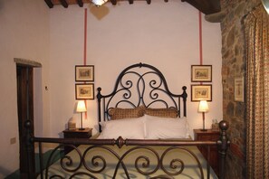 Ein Schlafzimmer mit einem hölzernen Bett, zwei Nachttischen mit Lampen, gerahmten Bildern an der Wand und einer Steinwand.