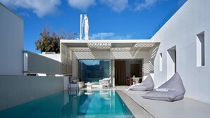 A modern outdoor swimming pool with a clear blue water surface, surrounded by white walls and a covered seating area with cushions. - Walk to Naousa | 5BR Pool Villa | Villa Yagha (46CJ+P7Q Naousa, Greece)