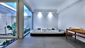 A modern spa room with a hot tub, a wooden bench, and a glass partition with plants. - Walk to Naousa | 5BR Pool Villa | Villa Yagha (46CJ+P7Q Naousa, Greece)