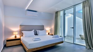 A modern bedroom with a large bed, bedside tables, an air conditioning unit, and a sliding glass door leading to a balcony. - Walk to Naousa | 5BR Pool Villa | Villa Yagha (46CJ+P7Q Naousa, Greece)