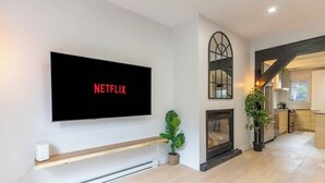 A modern living room with a mounted TV displaying 'NETFLIX,' a fireplace, and a kitchen area in the background.
