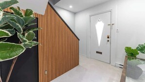 A modern hallway with a wooden accent wall, a geometric light fixture on the door, and potted plants.