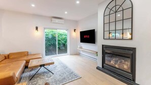A modern living room with a sofa, a coffee table, a fireplace, a TV, and a large window.