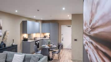 A modern kitchen with grey cabinets, a dining area with a table set for four, and a grey sofa with patterned cushions.