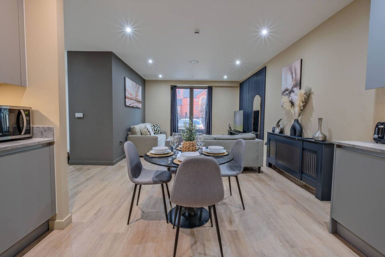 A modern kitchen with a dining area, featuring a central island, grey chairs, and a microwave on the counter.