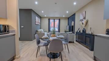 A modern kitchen with a dining area, featuring a central island, grey chairs, and a microwave on the counter.