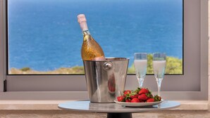 A bottle of champagne in a metal bucket, two glasses of champagne, and a plate of strawberries on a table by a window with a view of the sea. - White Stone Elegance with Pool, Jacuzzi & Golden Sunsets (Chania)