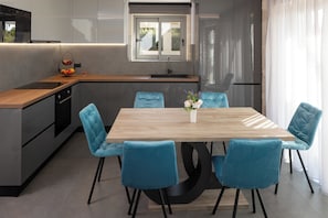 Eine moderne Küche mit Holzarbeitsplatte, integriertem Backofen und Spüle. Ein Esstisch mit vier blauen Stühlen und eine Vase mit Blumen sind ebenfalls vorhanden.