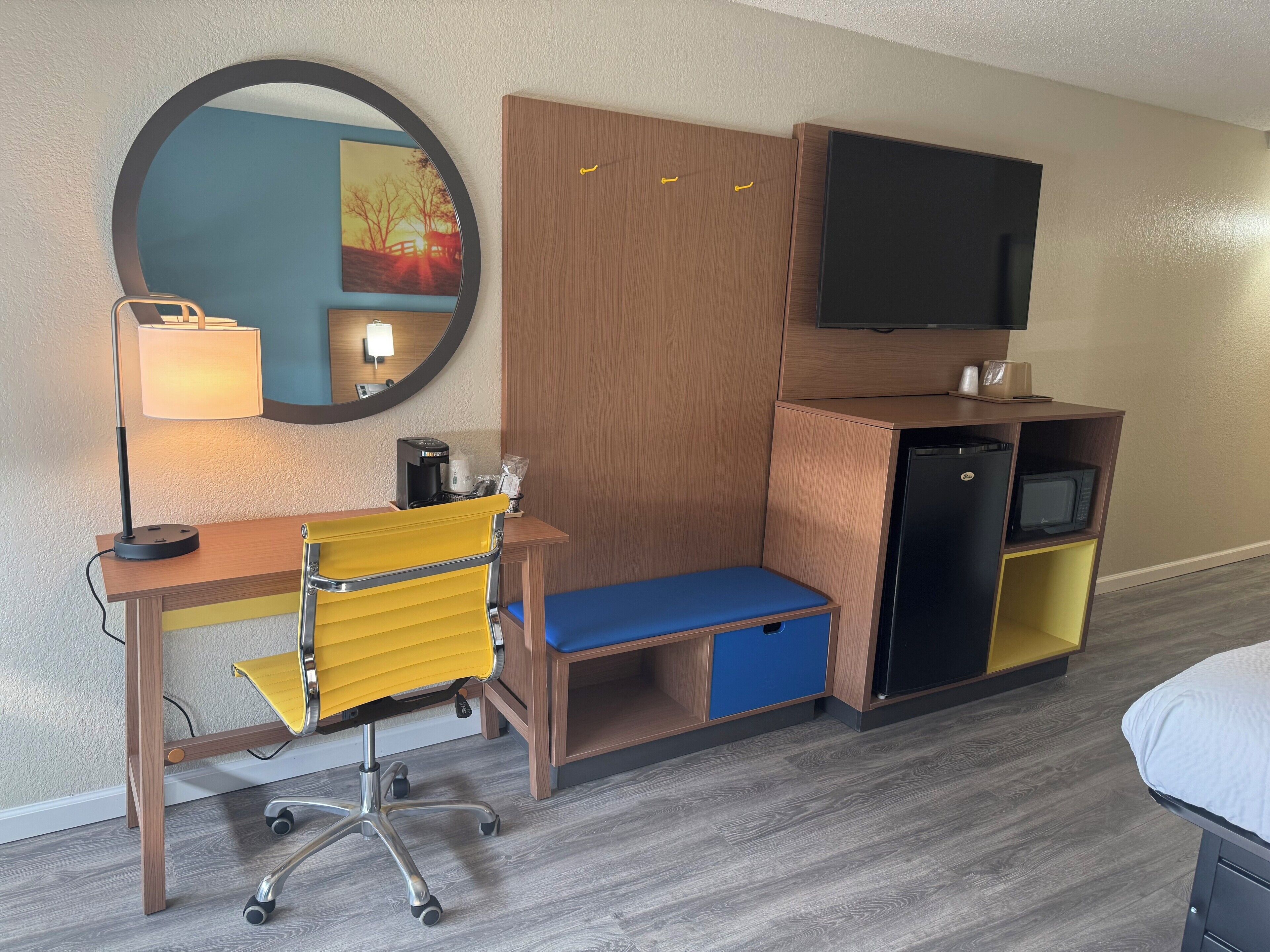 Ein kleines Hotelzimmer mit Schreibtisch, Stuhl und einer kompakten Küchenzeile.