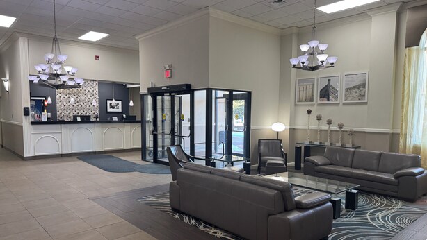 A hotel lobby with a reception desk, a revolving door, seating area with sofas, and a patterned rug. - Days Inn & Suites By Wyndham Festus (Festus)