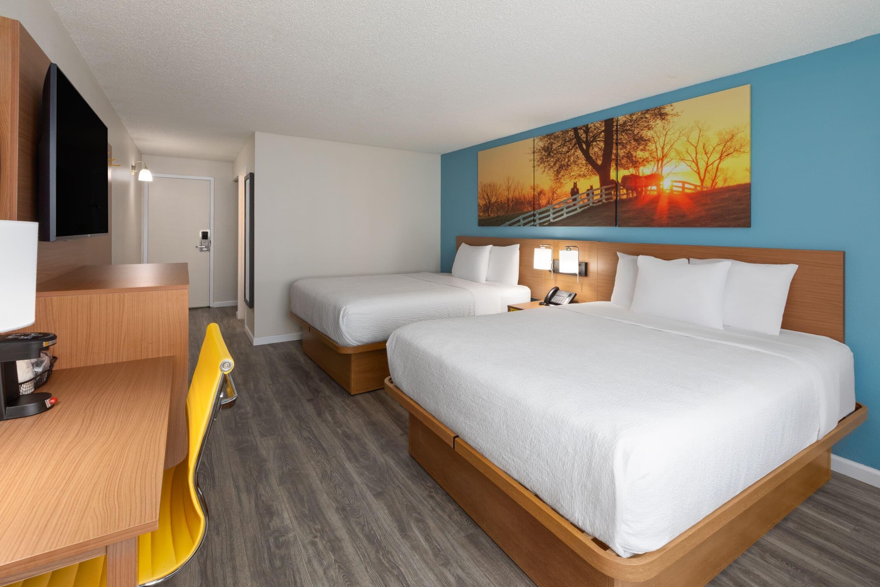A hotel room with two beds, a desk, a chair, a painting, and a TV.
