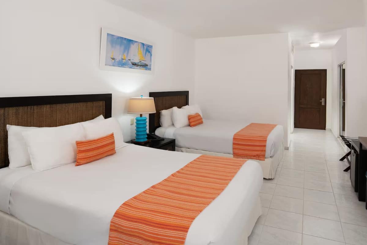 Une chambre d’hôtel avec deux lits, un tableau représentant des voiliers, une lampe et une porte donnant sur une autre pièce.