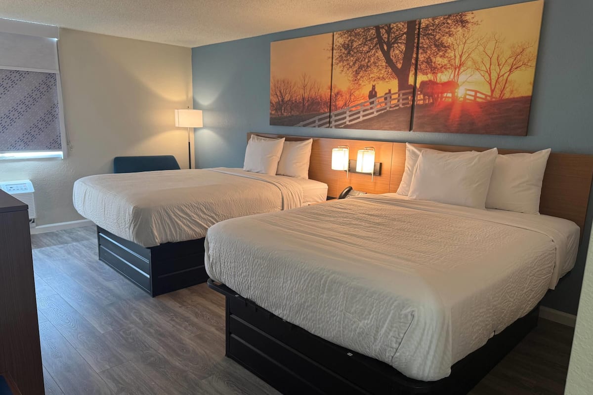 Une chambre d’hôtel avec deux lits, une table de chevet, une lampe et un grand tableau au mur.