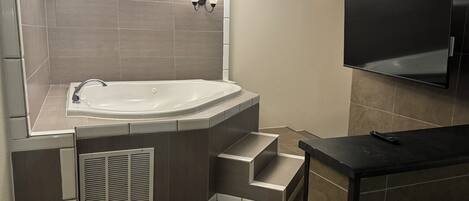 Une salle de bain moderne avec une baignoire sur pieds, un meuble-lavabo avec un miroir et un téléviseur à écran plat fixé au mur.