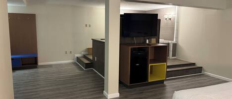 Un dormitorio moderno con cama, televisor y una pequeña kitchenette.