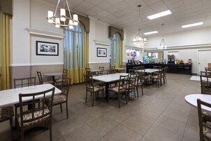 Un restaurante con varias mesas y sillas, una barra con máquina de café y cuadros en las paredes.