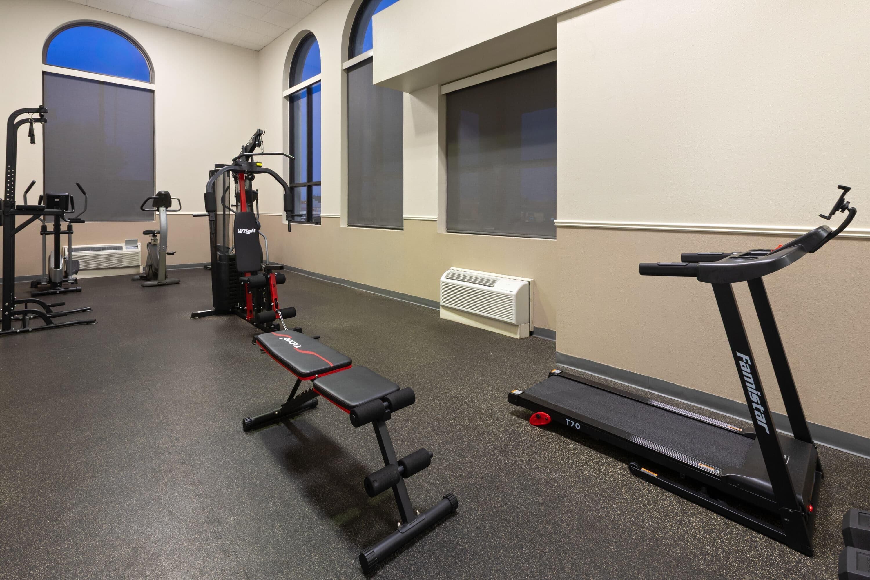A gym with exercise equipment including a bench, a treadmill, and weight machines.