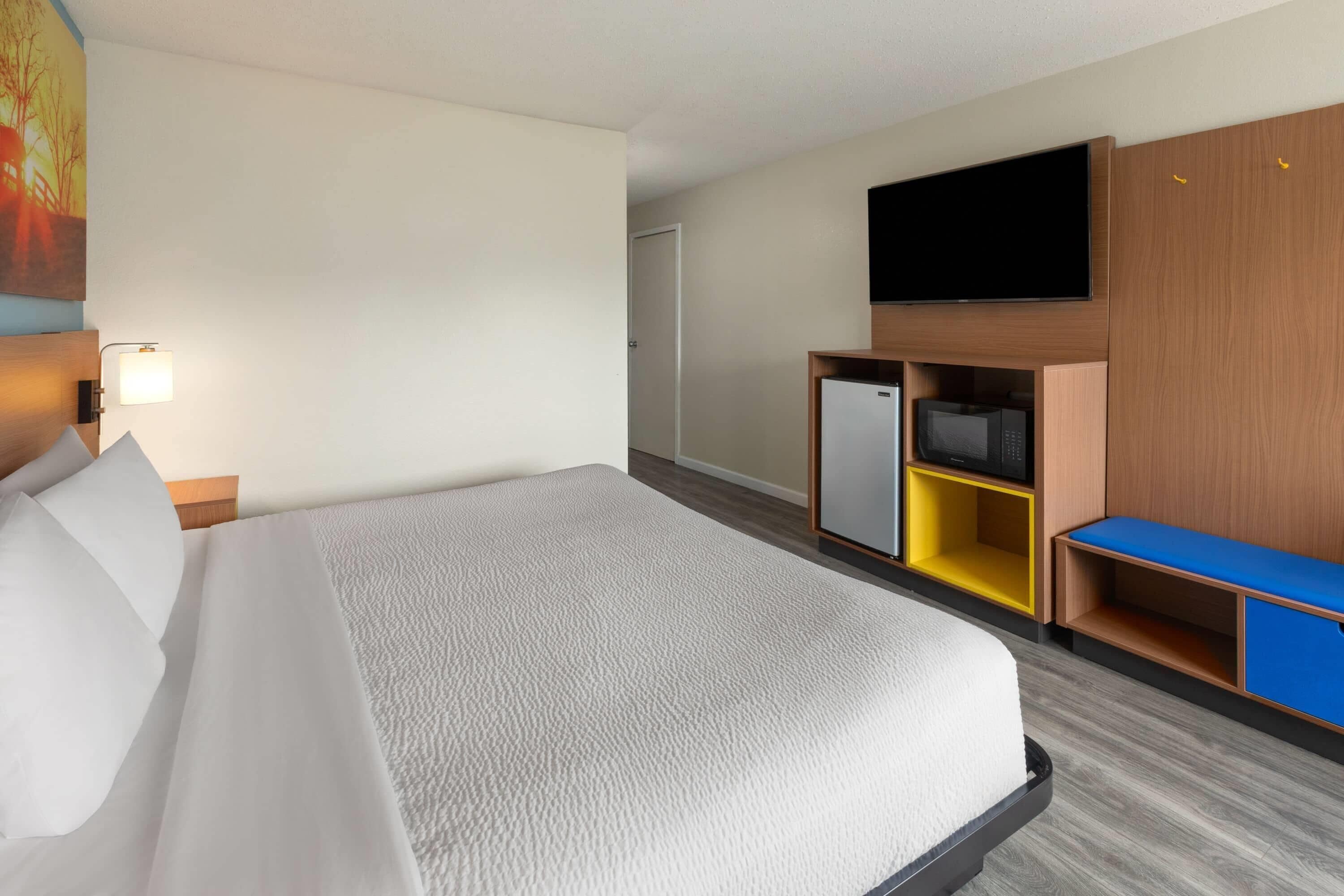 A hotel room with a bed, a TV, a minibar, and a desk.