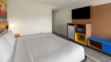 A hotel room with a bed, a TV, a minibar, and a desk.