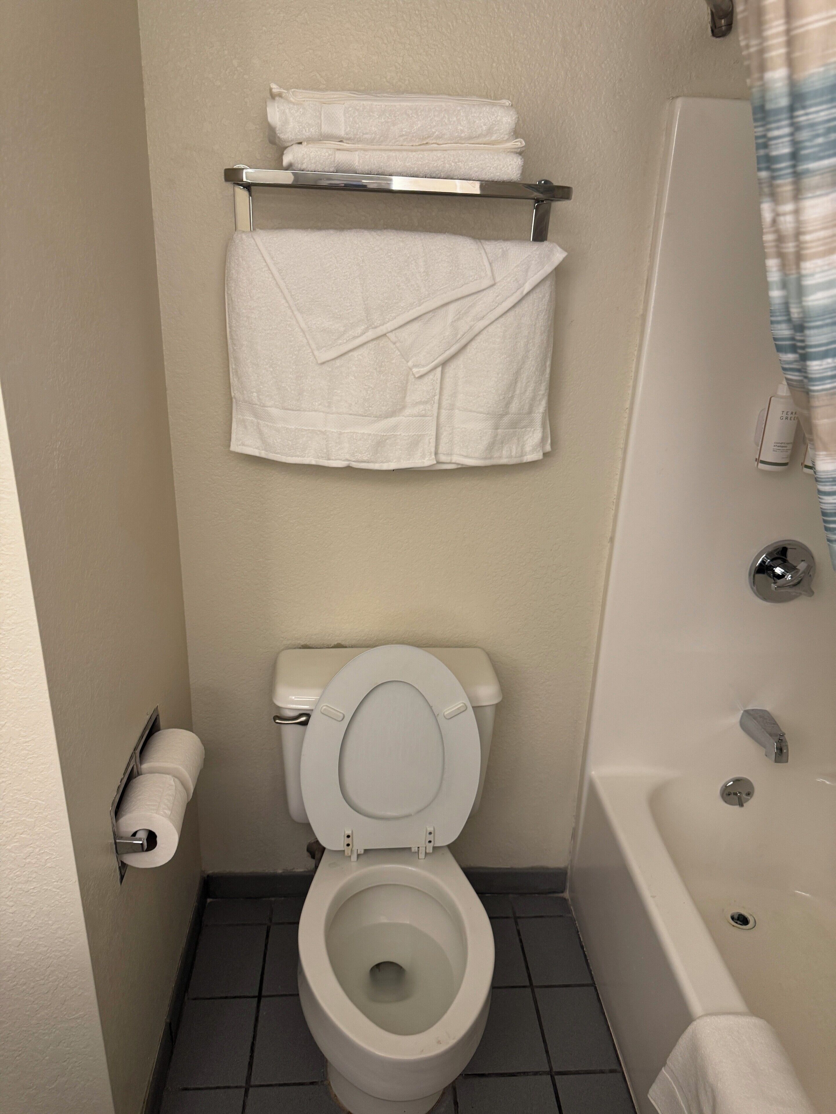 A bathroom with a toilet, a bathtub, and a towel rack with folded towels.