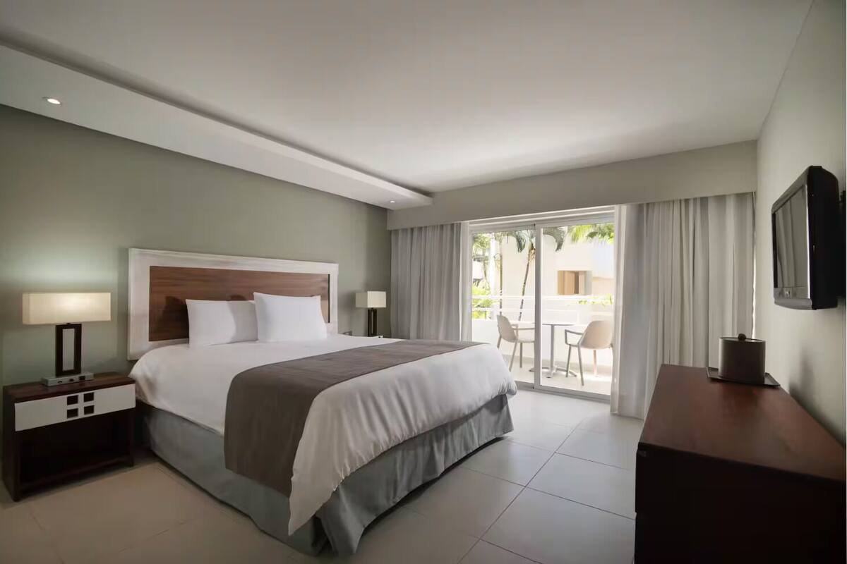 Une chambre d’hôtel comprenant un lit, une table de chevet, un bureau, une chaise et un balcon avec vue.