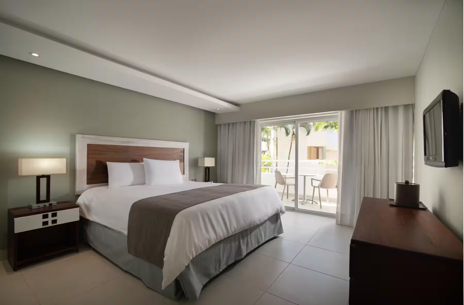 A hotel room with a bed, a nightstand, a desk, a chair, and a balcony with a view.