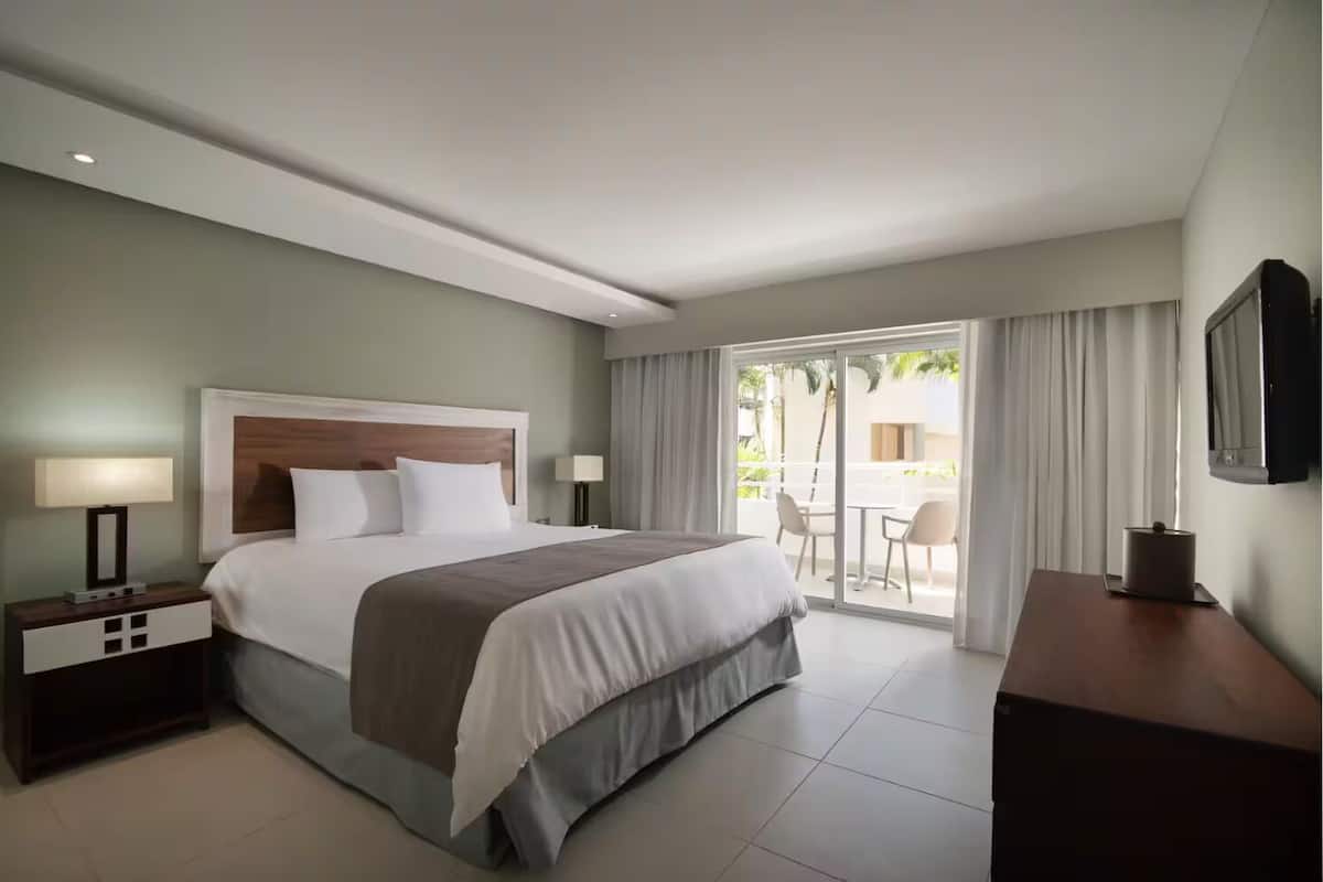 Une chambre d’hôtel comprenant un lit, une table de chevet, un bureau, une chaise et un balcon avec vue.