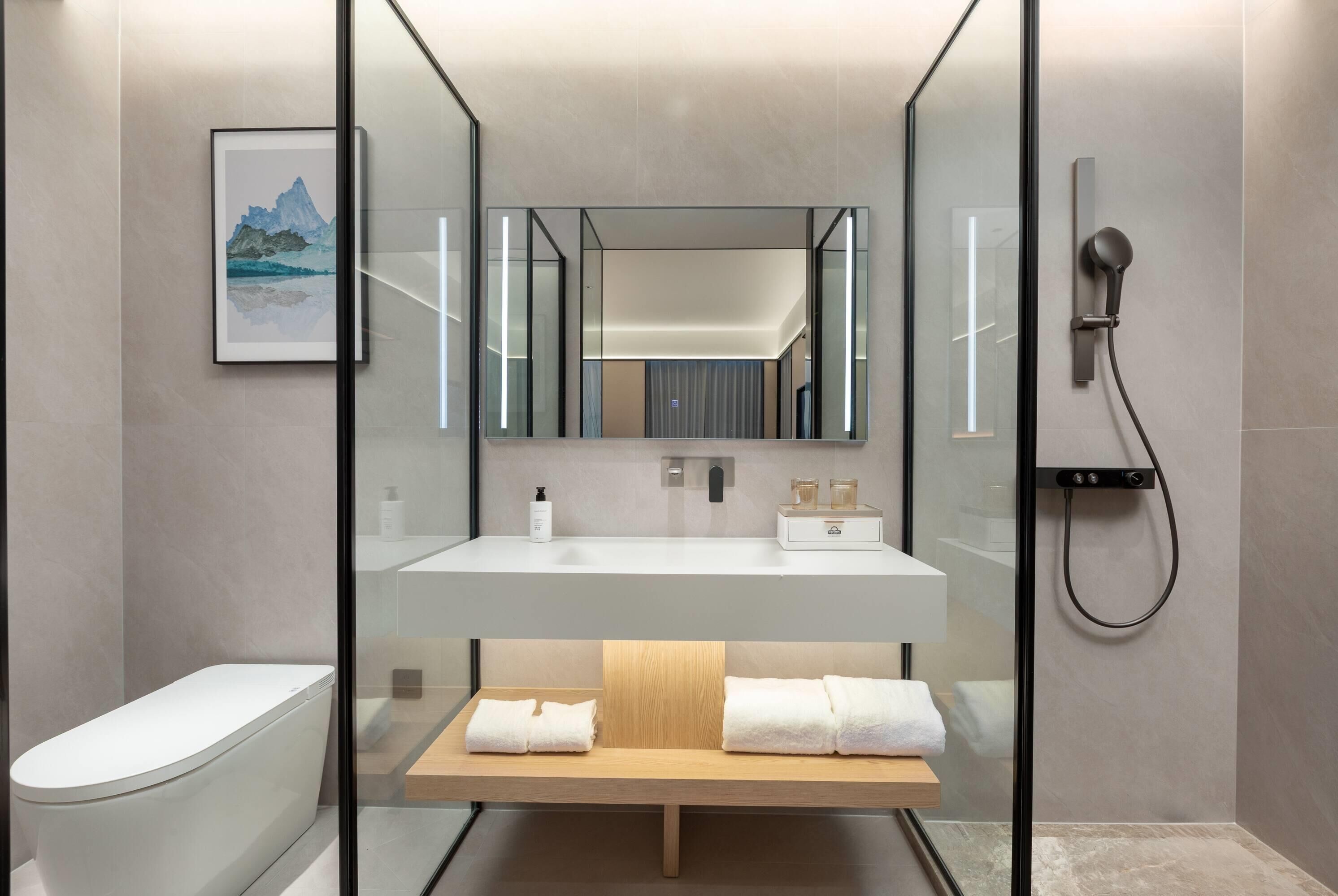 A modern bathroom with a glass-enclosed shower, a white sink, and a wooden bench with towels.