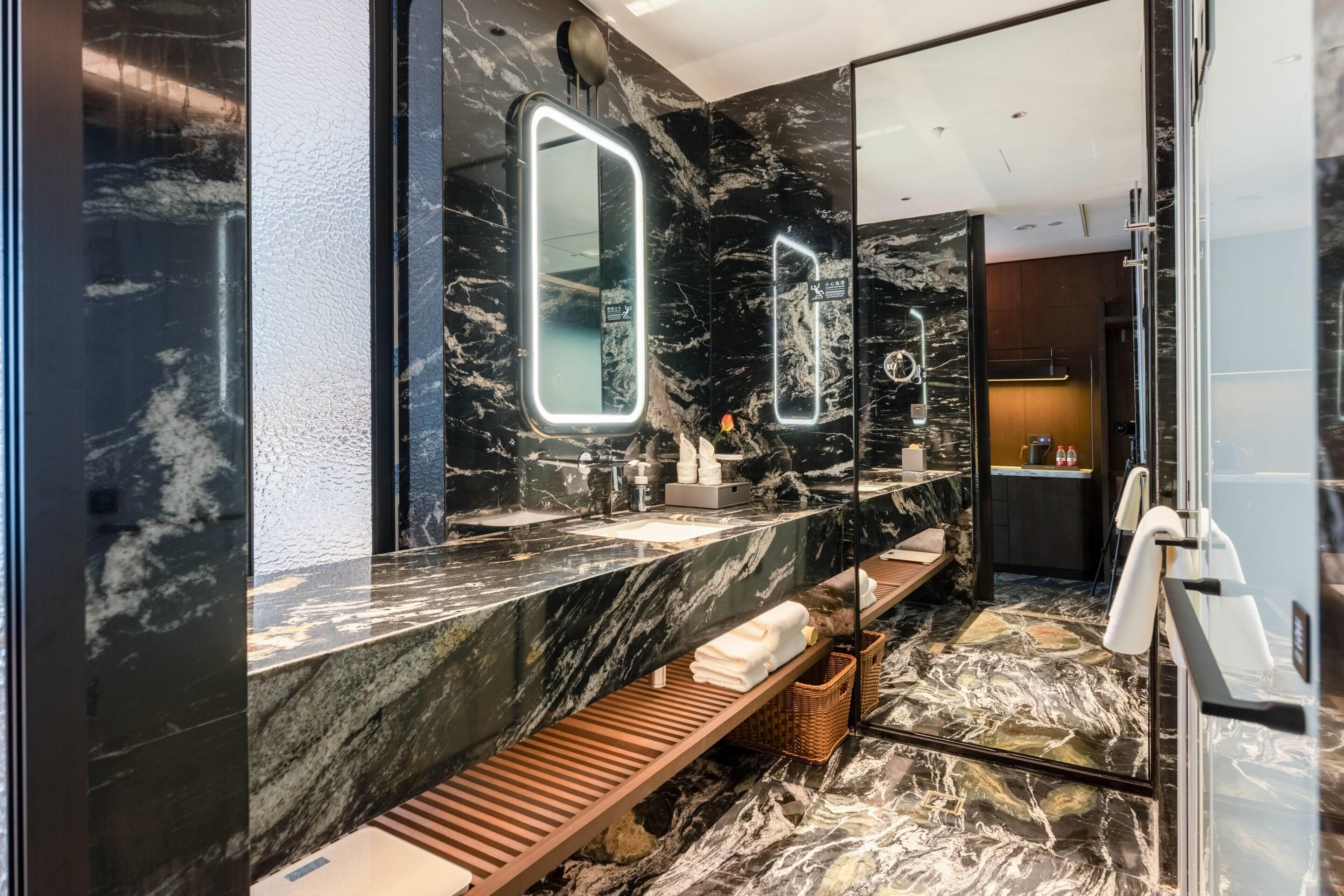 Un baño moderno con tocador de mármol, un banco, toallero y espejo con iluminación integrada.