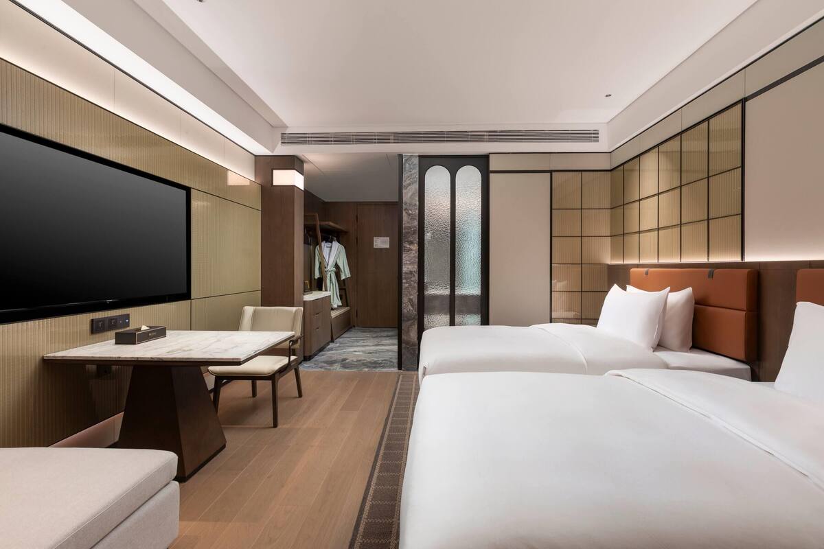 Habitación de hotel con televisor de pantalla plana, mesa de comedor, dos camas y vestidor.