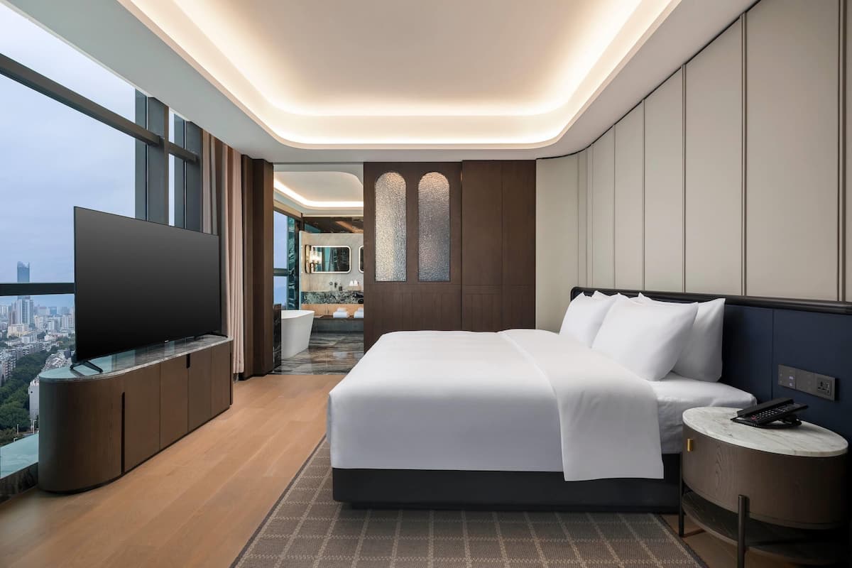 Una habitación de hotel moderna con una cama grande, un televisor de pantalla plana, una mesita redonda y vistas a la ciudad.