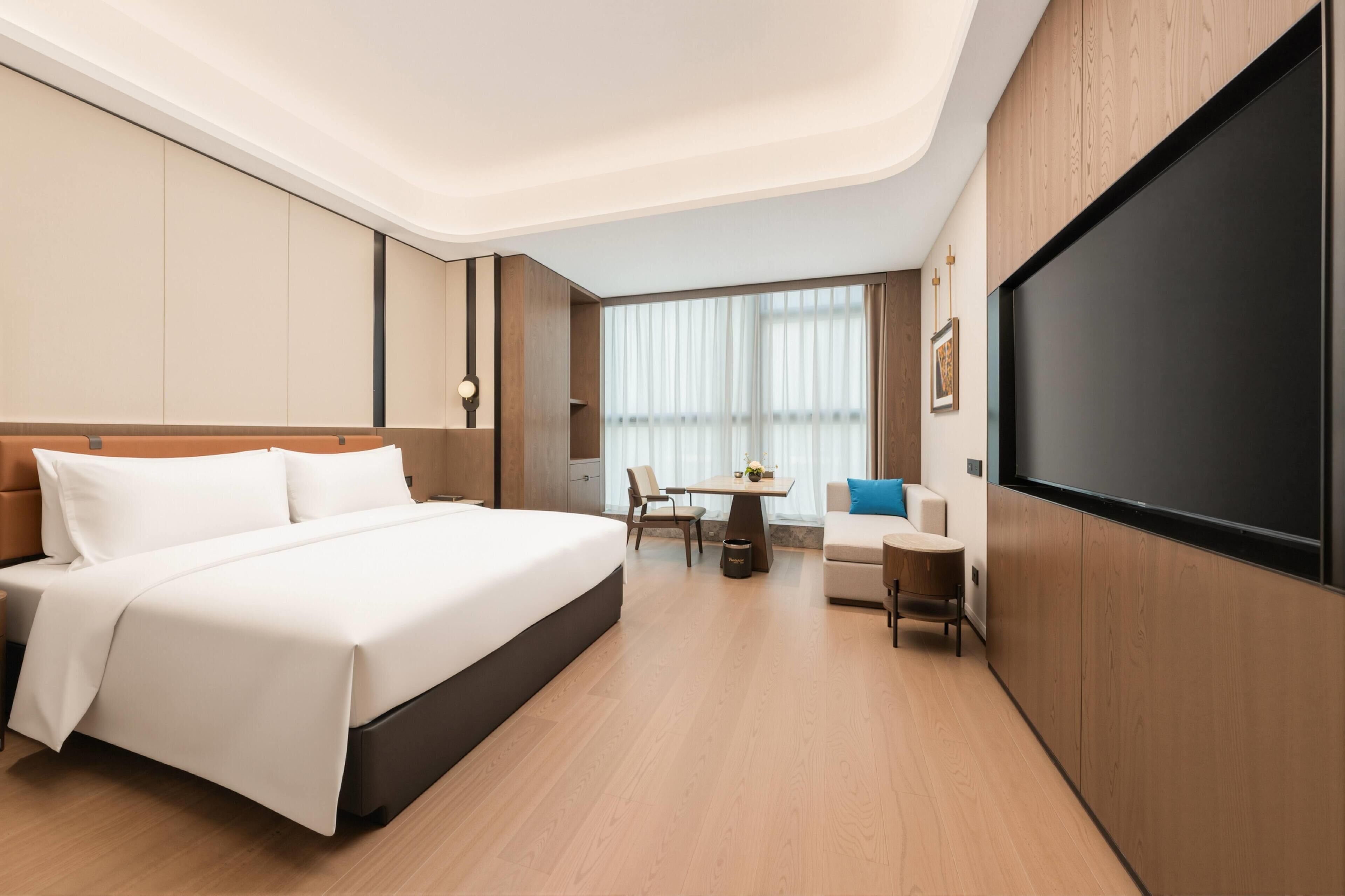 A modern hotel room with a large bed, a desk, a chair, and a TV.