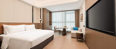 A modern hotel room with a large bed, a desk, a chair, and a TV.