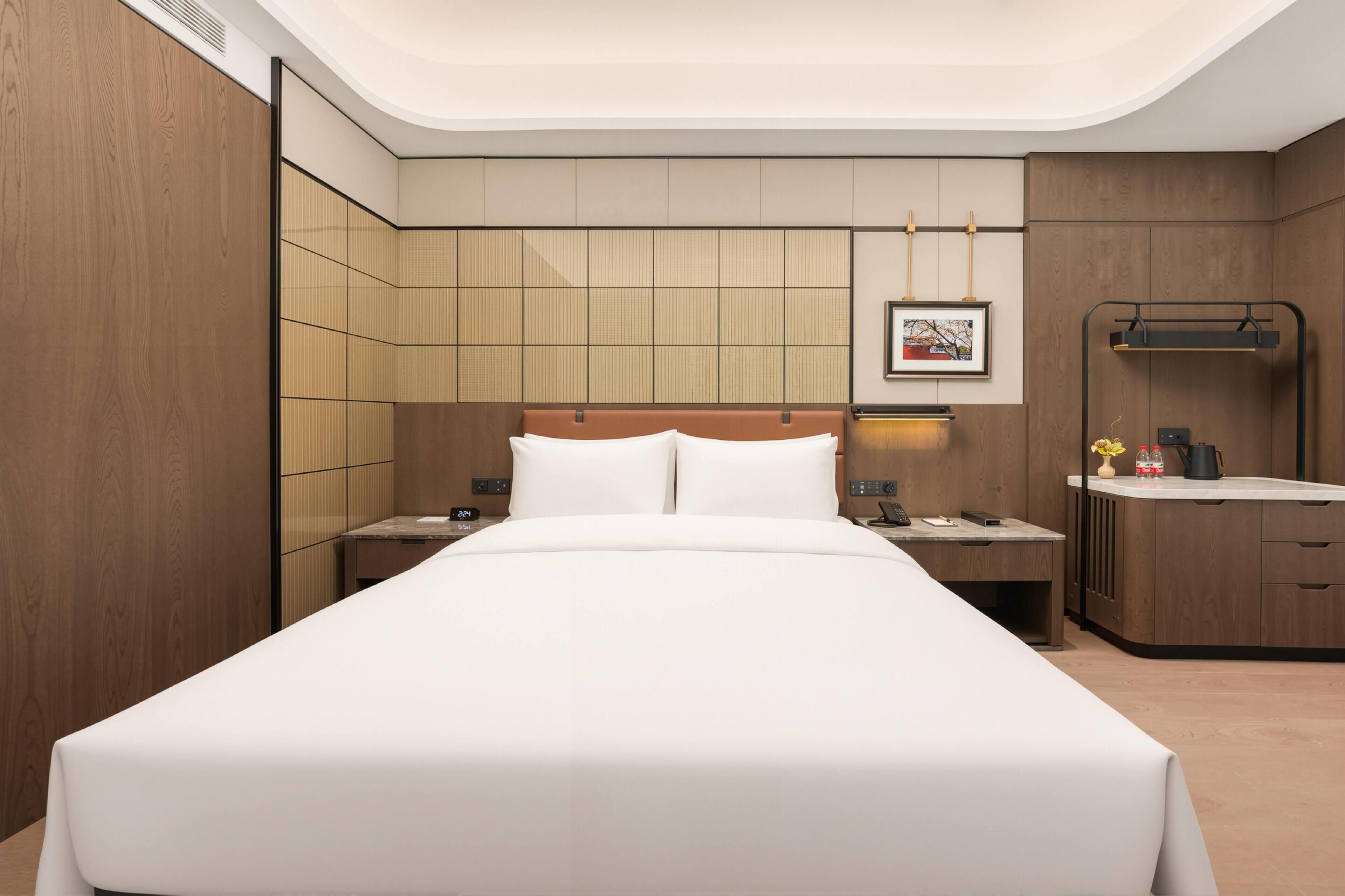 Una camera d'albergo moderna con un letto grande, comodini, una piccola scrivania e un armadio a muro.
