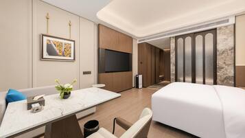 Una habitación de hotel moderna con cama, televisión, escritorio y un florero, y un ventanal amplio.