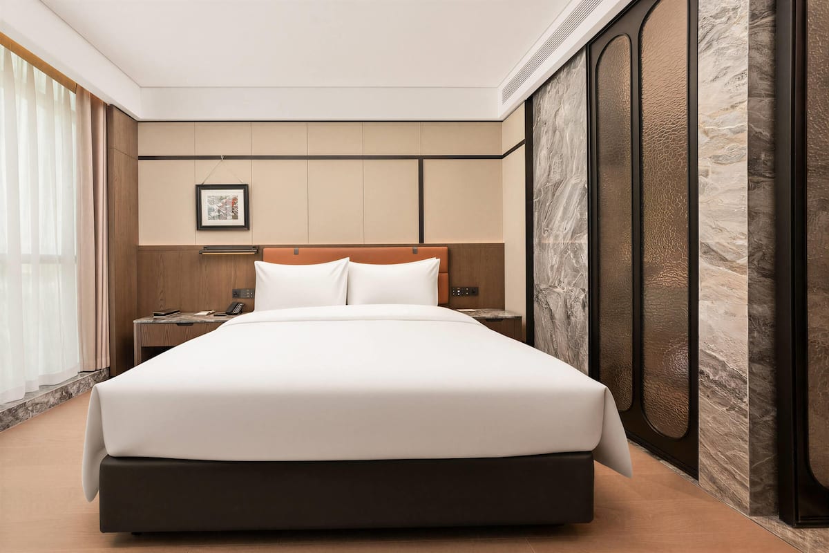 Una habitación de hotel moderna con una cama grande, una mesita de noche y un teléfono instalado en la pared.