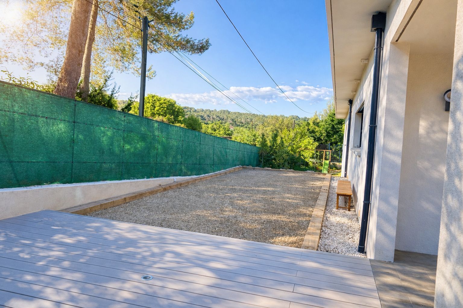 A covered outdoor area with a wooden deck, a green wall, and a view of a forested hillside.