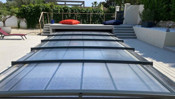 Een dakterras met glazen dak, houten vloer en buitenterras.