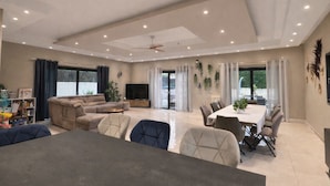 A spacious living area with a sofa, dining table, and chairs. There is a TV and a ceiling fan. - Villa with Pool, Petanque, Sauna, Steam & children's facilities - French Riviera (Roquefort Les Pins)