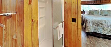 Ein Zimmer mit Holzvertäfelung, einer Duschkabine aus Glas, einem Bett mit gemustertem Überwurf und einem sichtbaren Fenster.