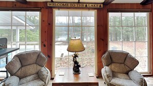 Een blokhutinterieur met een bordje 'Welcome to the Lake', twee fauteuils, een lamp en een houten tafel.